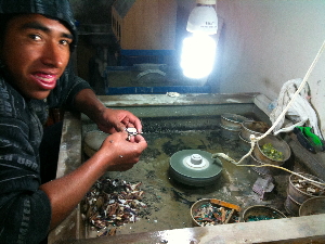 Silversmith grinding semi-precious stones and shells into small pieces and gluing them into silver jewelry with tree resin